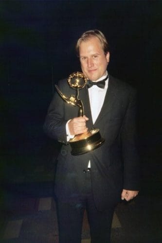 LiveTube - A man in a tuxedo holds an Emmy Award trophy, standing against a dark background.
