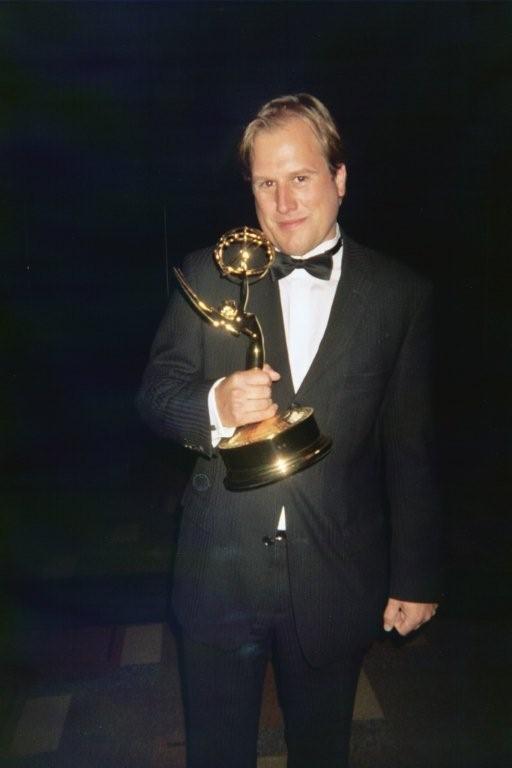 LiveTube - A man in a tuxedo holds an Emmy Award trophy, standing against a dark background.