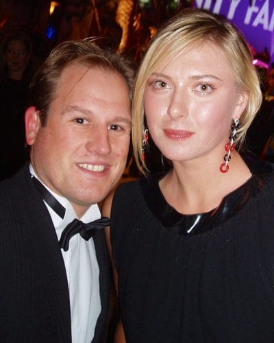 LiveTube - A man in a tuxedo and a woman in a black dress pose together at an indoor event with colorful lighting in the background.