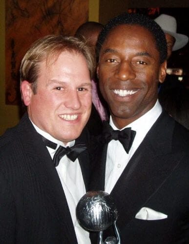 LiveTube - Two men in tuxedos pose together; the man on the right holds a silver award trophy and smiles at the camera.