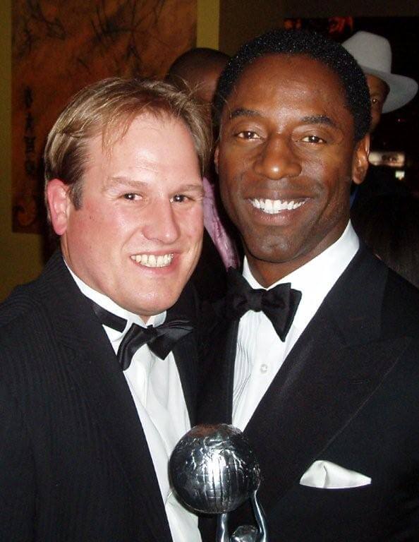 LiveTube - Two men in tuxedos pose together; the man on the right holds a silver award trophy and smiles at the camera.