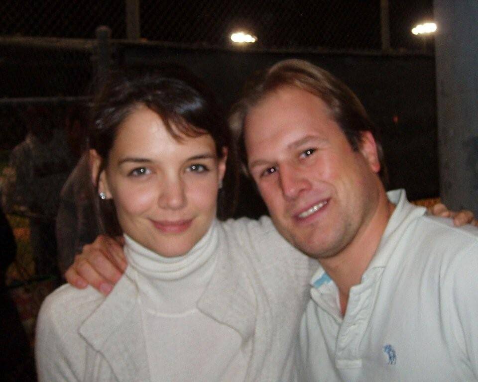 LiveTube - A woman and a man pose closely together and smile at the camera in an outdoor nighttime setting with a chain-link fence in the background.