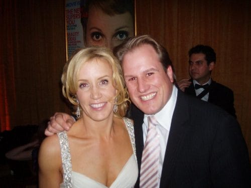 LiveTube - Two people dressed in formal attire pose and smile for a photo at an indoor event. A man in a tuxedo stands in the background.