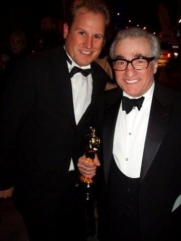 LiveTube - Two men in tuxedos pose for a photo. One man is holding an Oscar statuette. They are both smiling and standing close together at what appears to be an event.